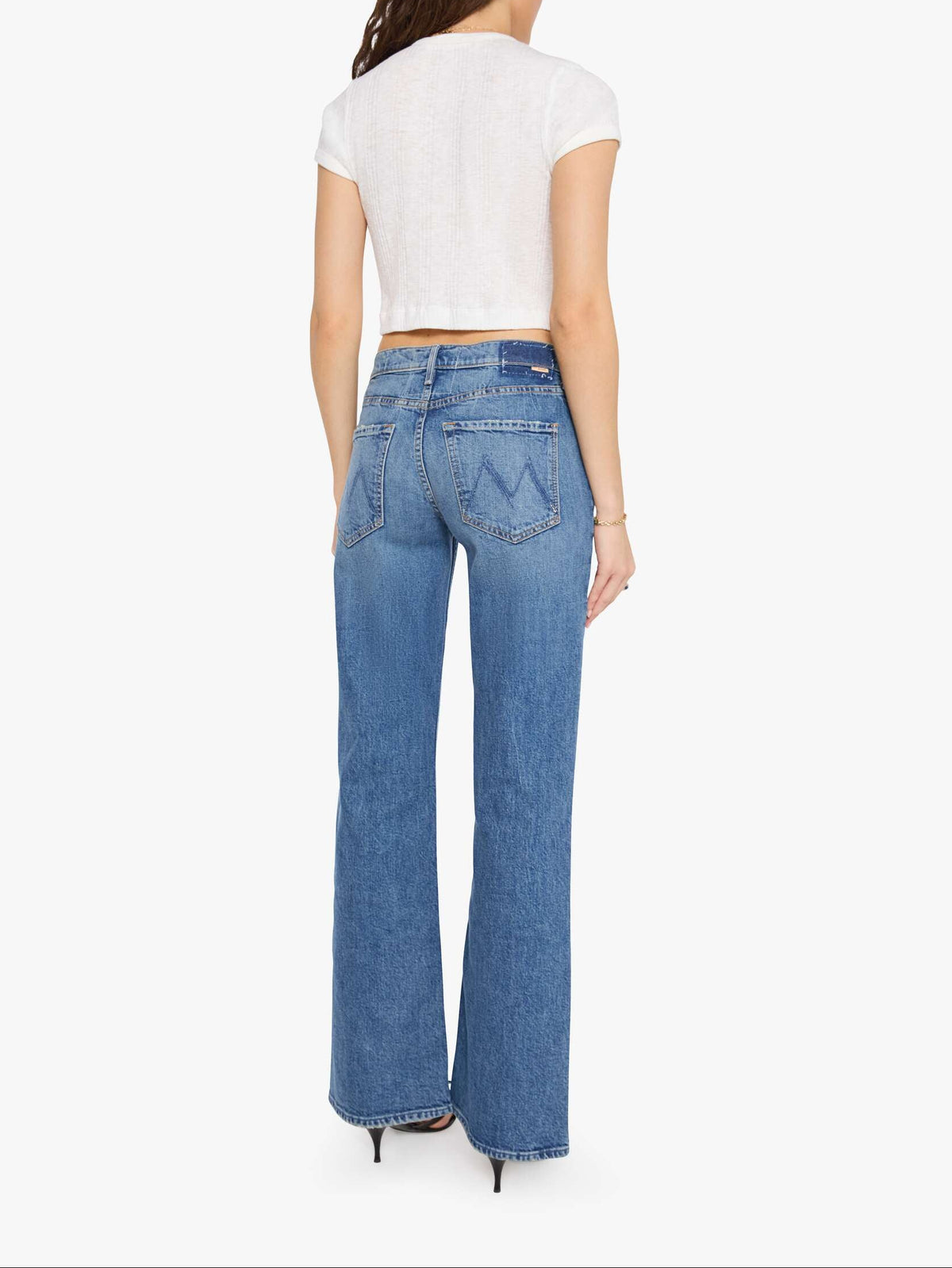 A woman viewed from the back wearing a white cropped short-sleeve top and blue wide-leg jeans with a distinctive W-shaped pocket on the back, set against a plain white background.