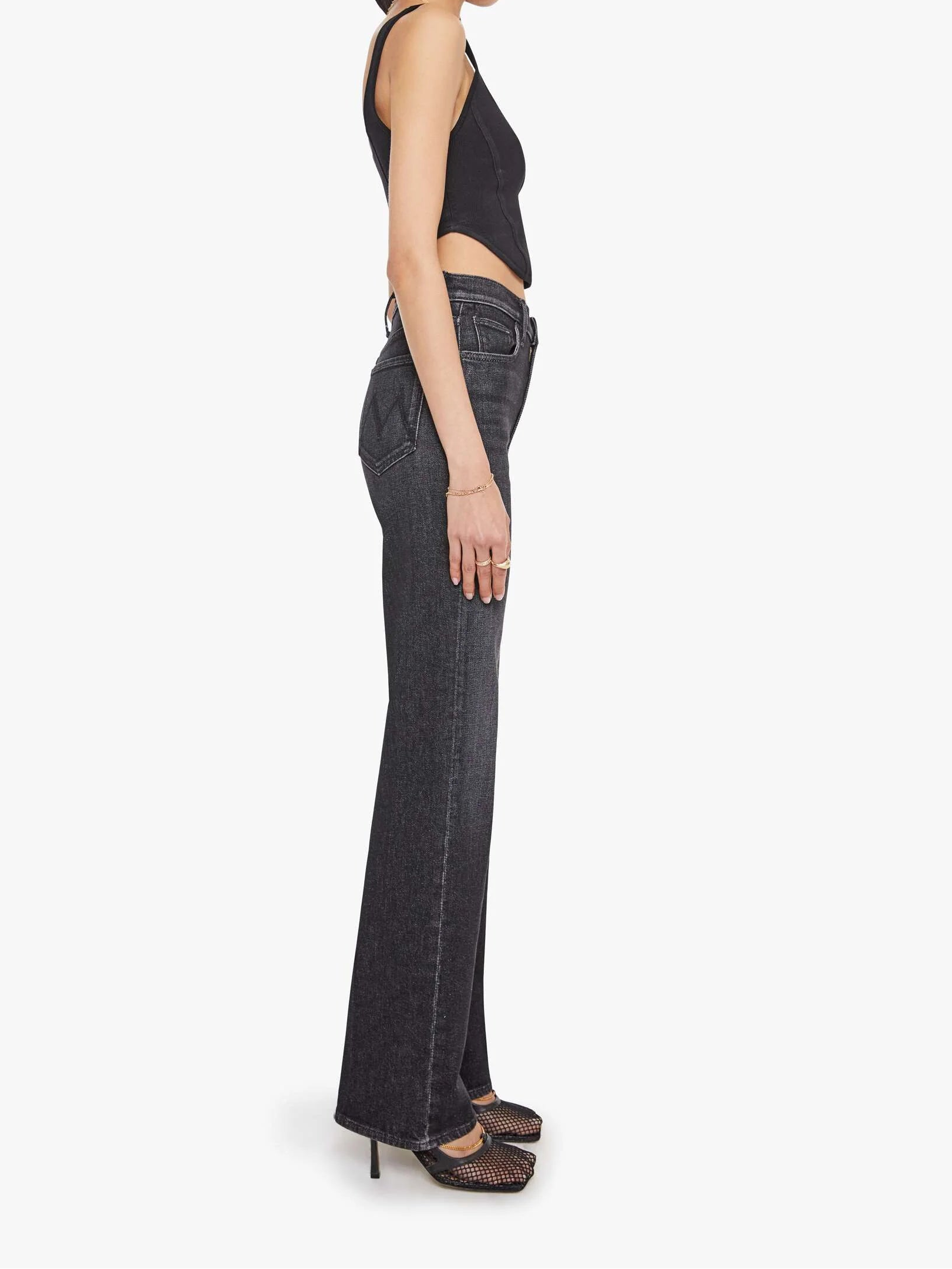 Woman wearing black top and dark jeans on a white background, side view