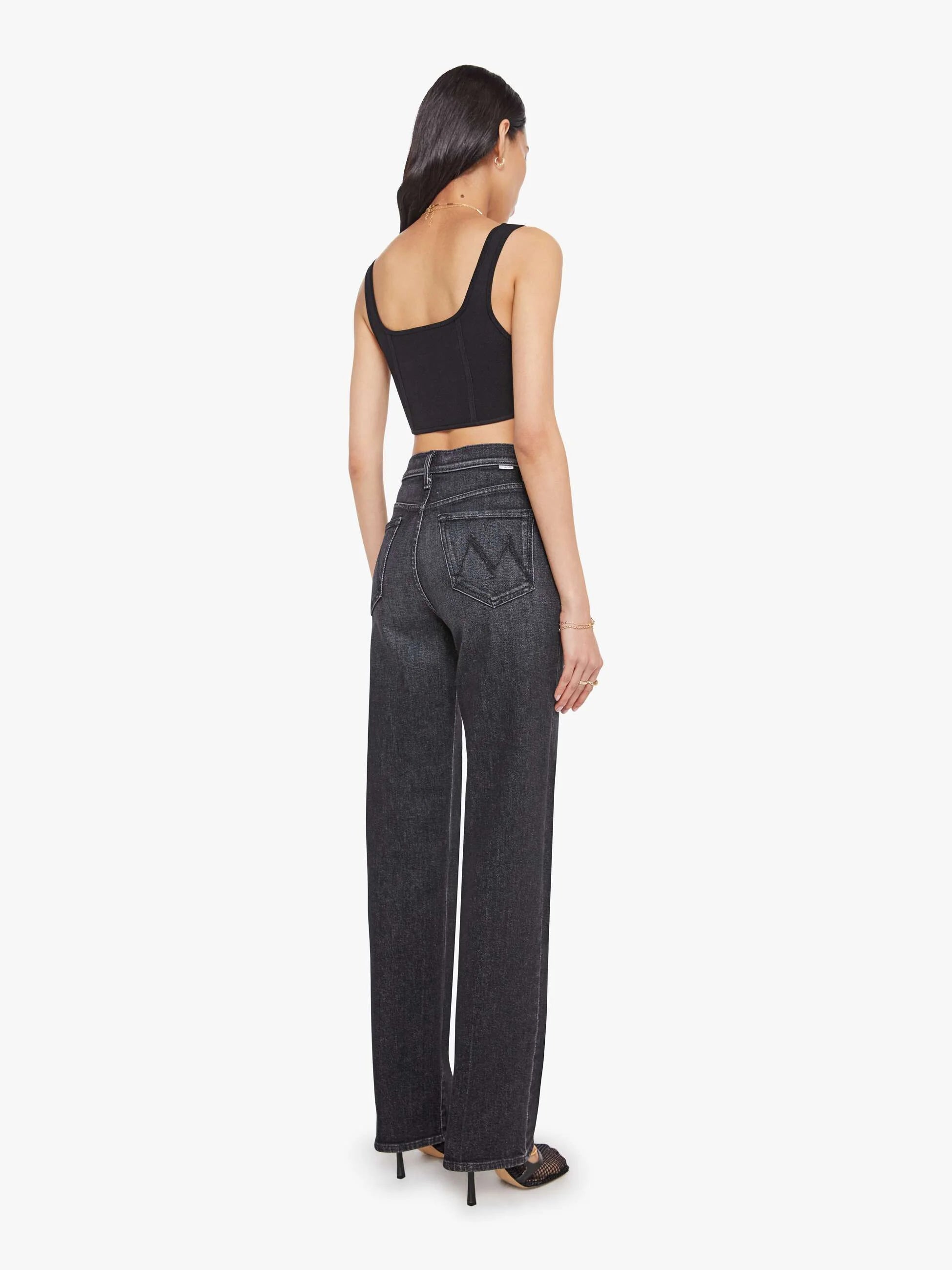 Woman wearing black high-waisted jeans and a black crop top on a white background, back view