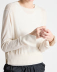 Person wearing a cream sweater and black pants on a white background
