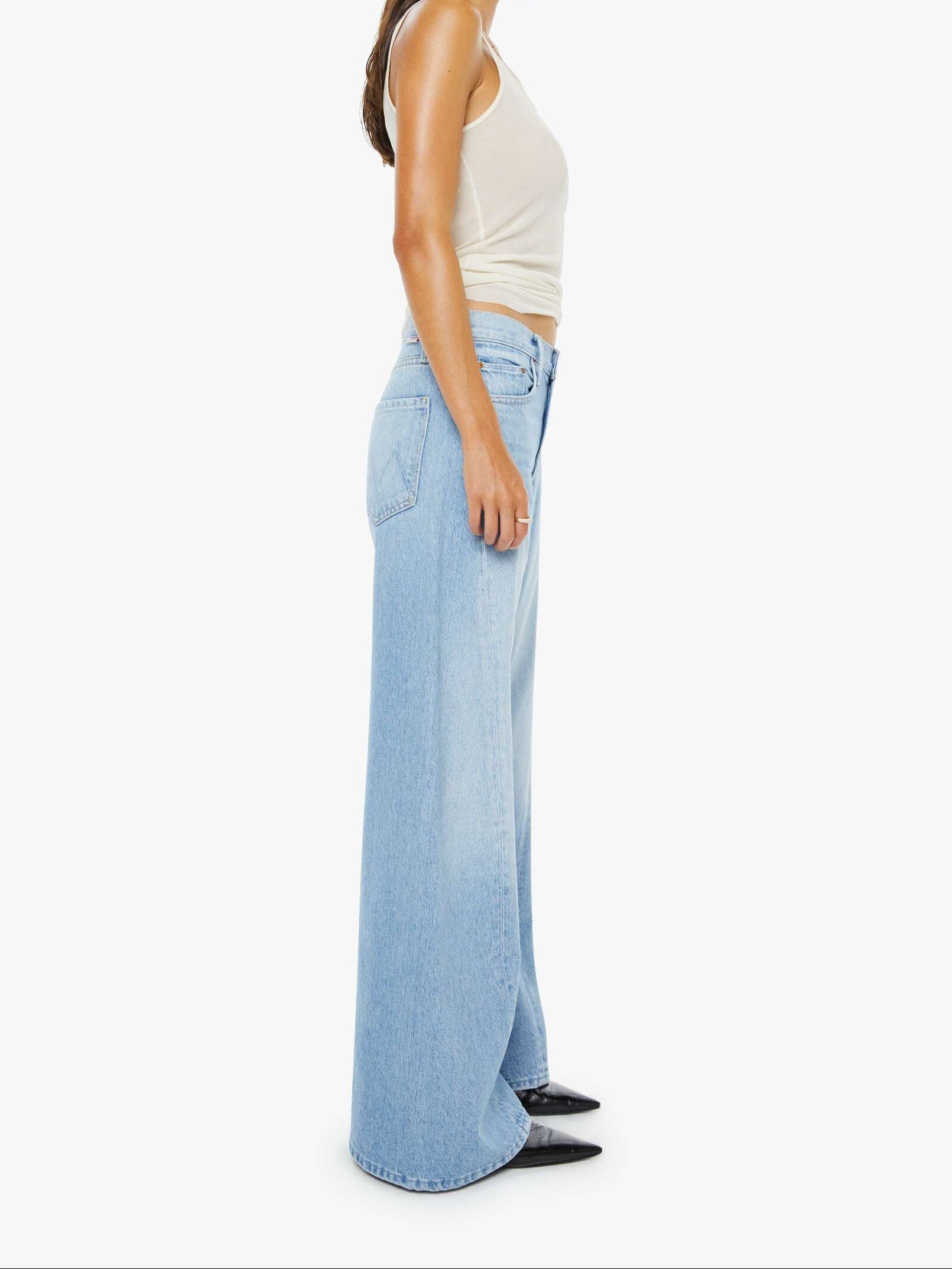 Woman wearing light blue wide-leg jeans and a white top on a white background