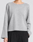 model wearing a grey long sleeve sweater and black pants on a grey background 