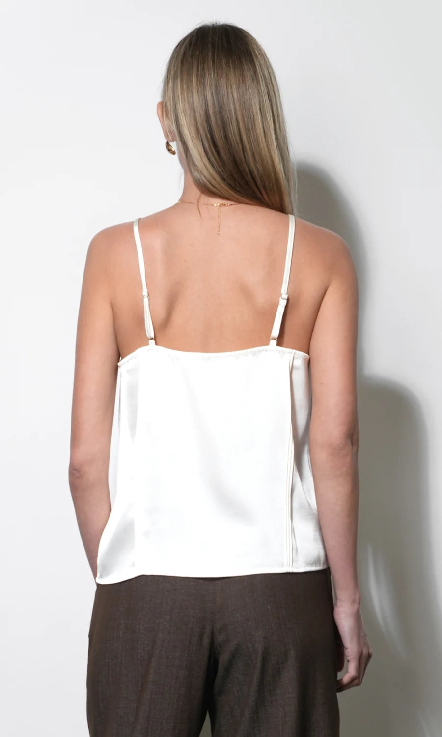 Woman wearing a white top and brown pants against a plain background