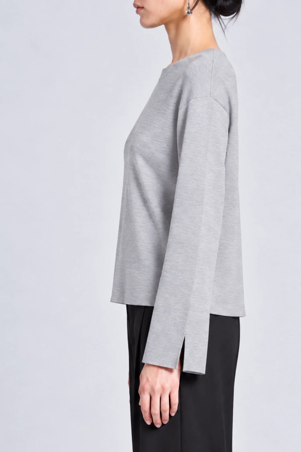 model wearing a grey long sleeve sweater and black pants on a grey background, side view