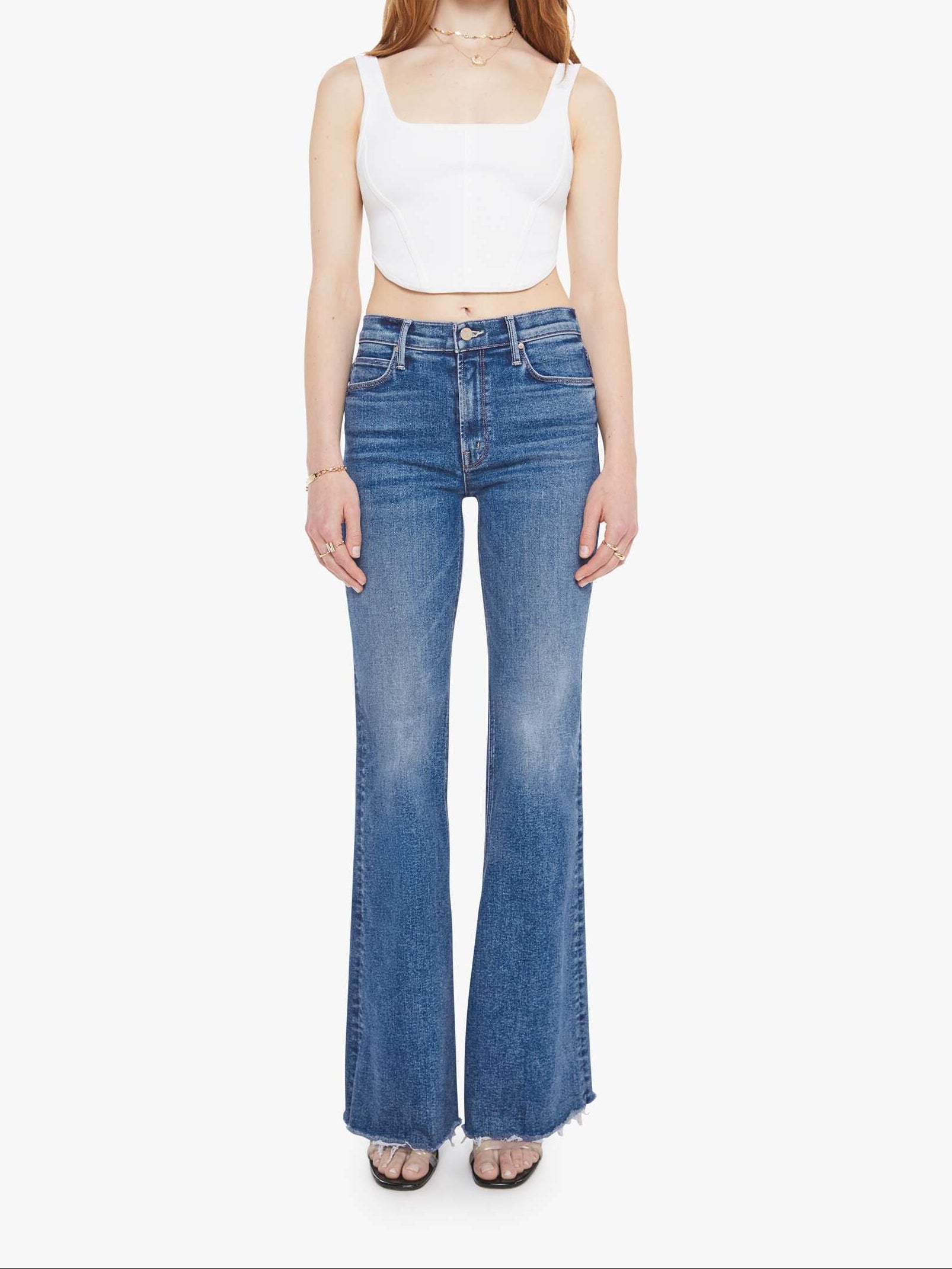 Woman wearing blue flared jeans and a white top on a white background, front