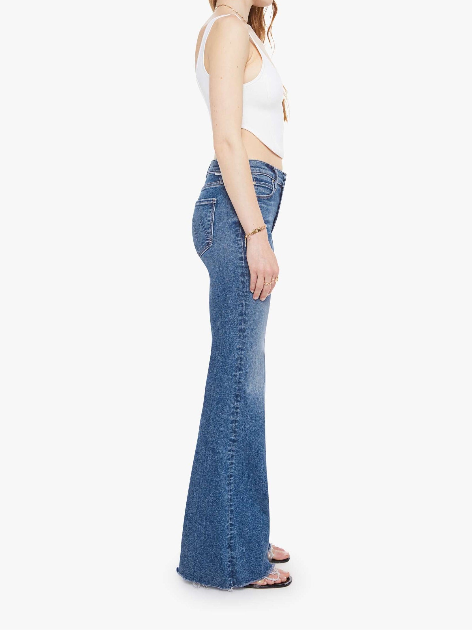 Woman wearing blue flared jeans and a white top on a white background, side