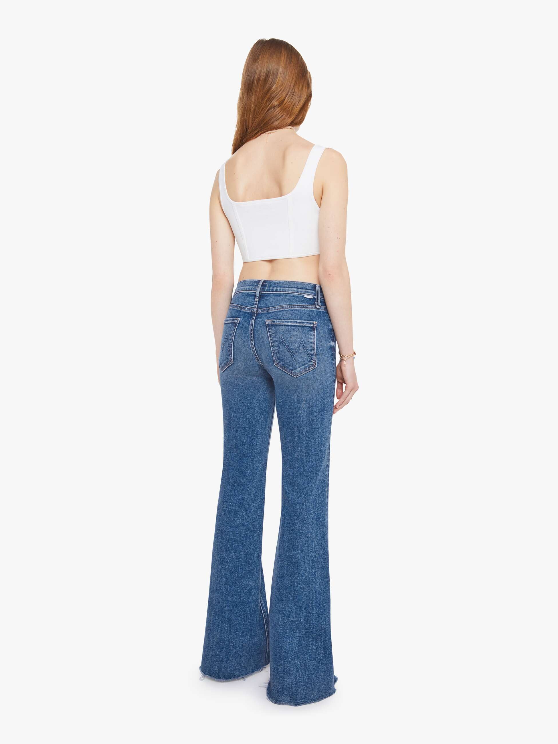 Woman wearing blue flared jeans and a white top on a white background, back