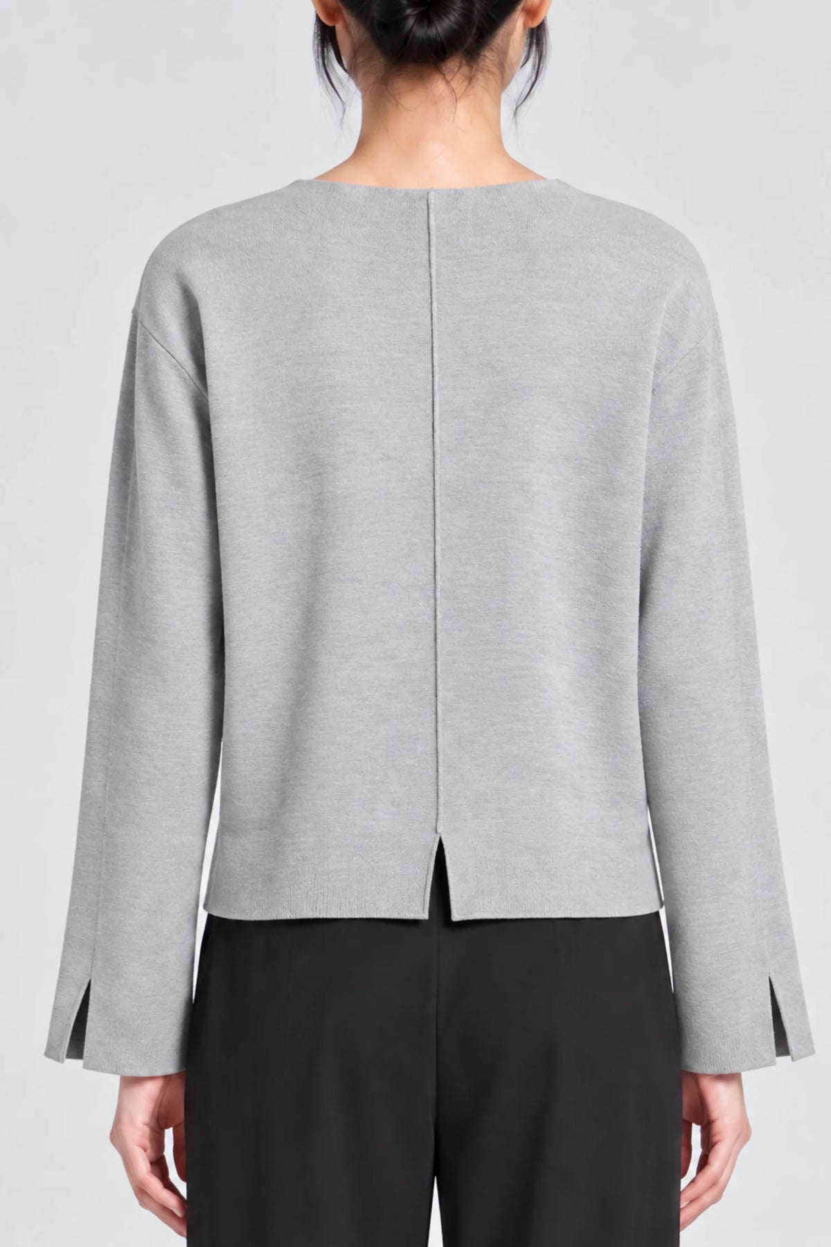model wearing a grey long sleeve sweater and black pants on a grey background, back view with back vent slit and wrist 