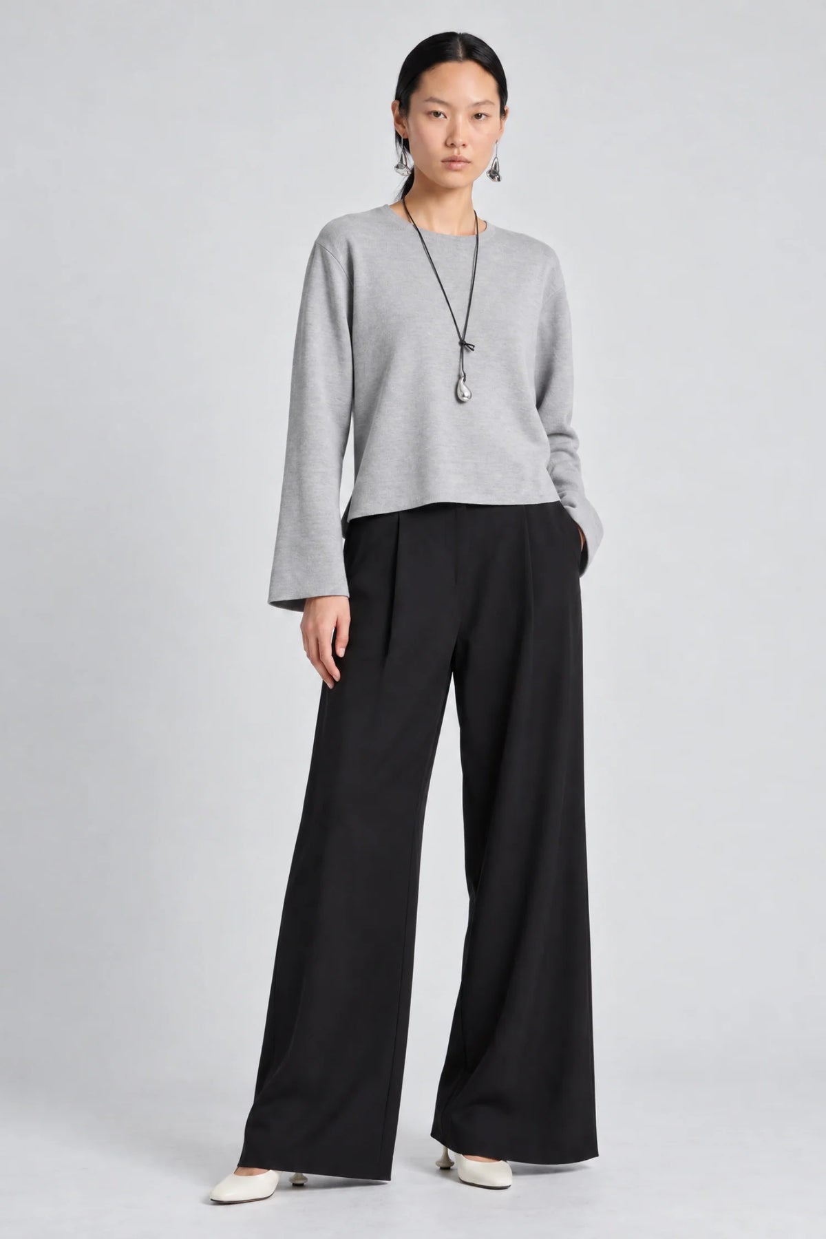 model wearing a grey long sleeve sweater and black pants on a grey background 