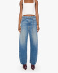 A model stands against a light gray studio background wearing a white ribbed crop top, wide-leg blue denim jeans, and dark burgundy pointed-toe heels.