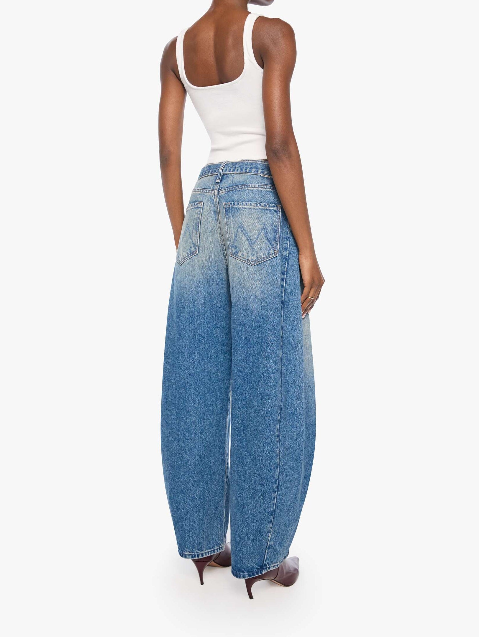 A model shown from the back wearing wide-leg blue denim jeans with a faded wash, a white tank top, and brown pointed-toe heels against a plain white studio background.