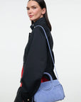 A model in a black jacket is shown from the side, carrying a light blue suede shoulder bag with a matching strap against a plain white studio background.
