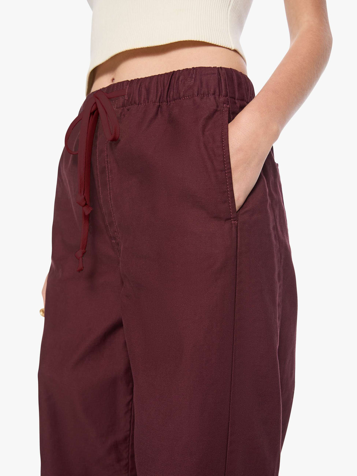 A close-up of a person wearing burgundy drawstring wide-leg pants with side pockets, paired with a cream ribbed crop top against a plain white background.