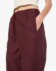 A close-up of a person wearing burgundy drawstring wide-leg pants with side pockets, paired with a cream ribbed crop top against a plain white background.