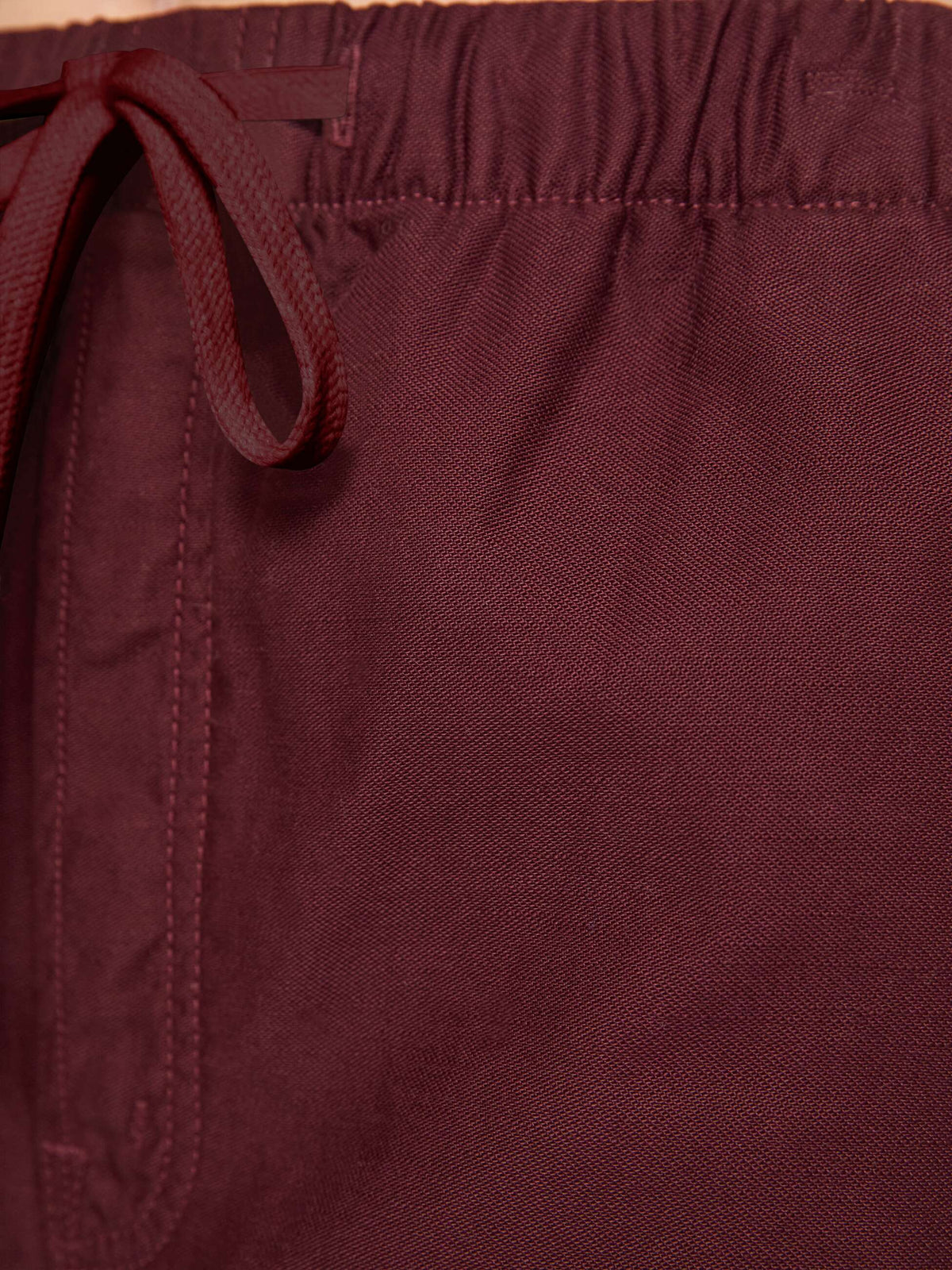 Close-up of a pair of burgundy drawstring shorts showing the textured fabric, waistband, and drawstring loop.