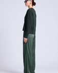A woman in side profile wearing a dark green long-sleeve top and matching wide-leg trousers against a light gray studio background.