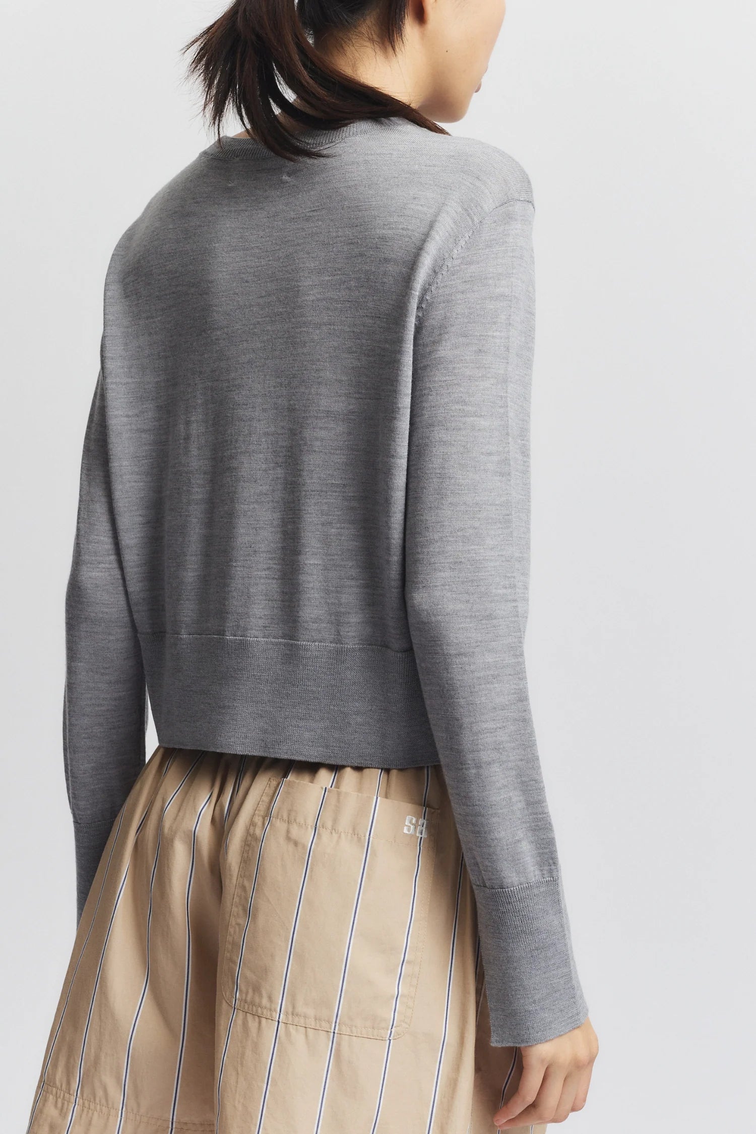 Person wearing a gray sweater and beige striped pants on a light gray background