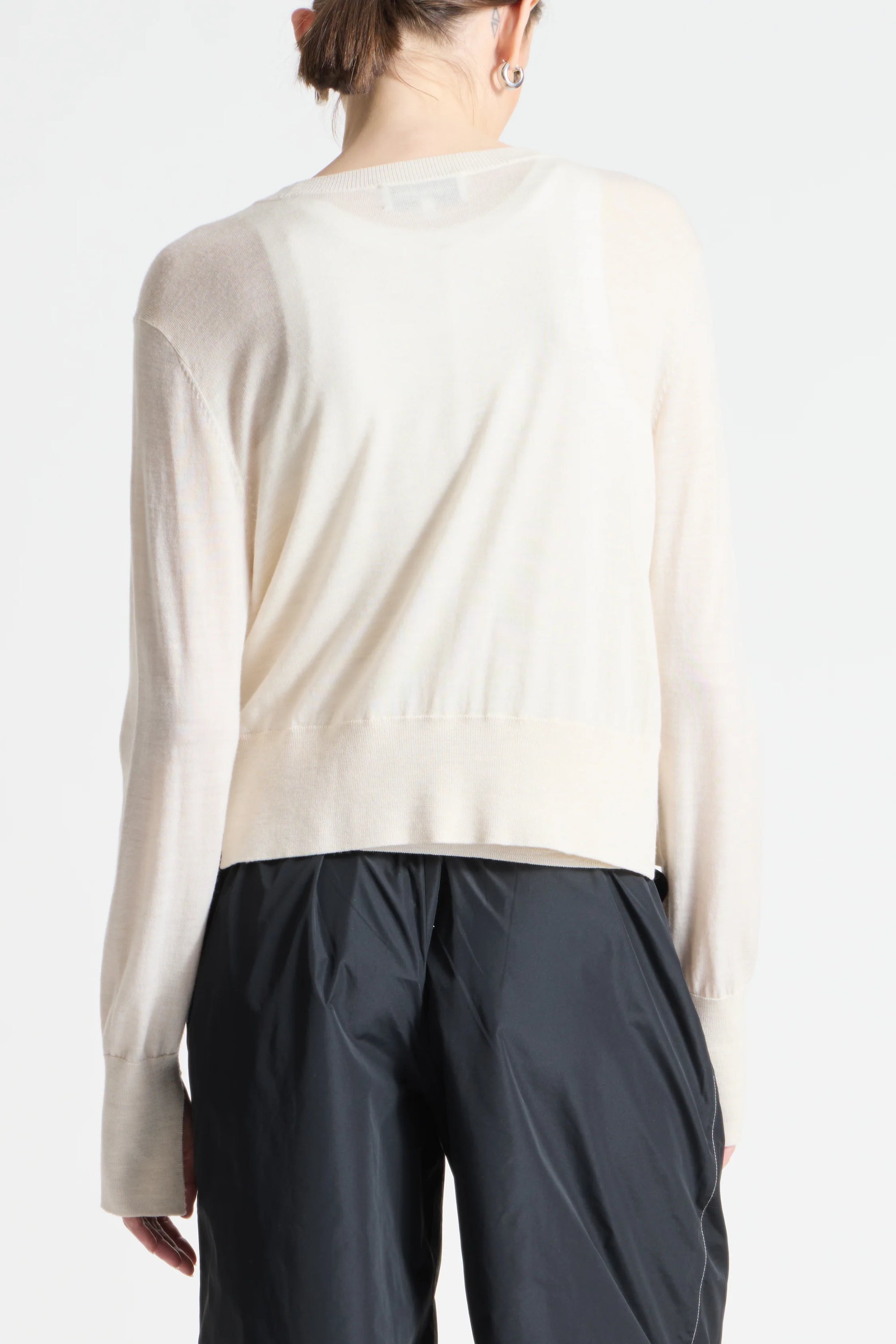 Person wearing a beige long-sleeve top and dark pants on a white background