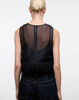 A model viewed from the back wearing a black sheer mesh sleeveless top with fringe trim and dark blue jeans against a plain white studio background.