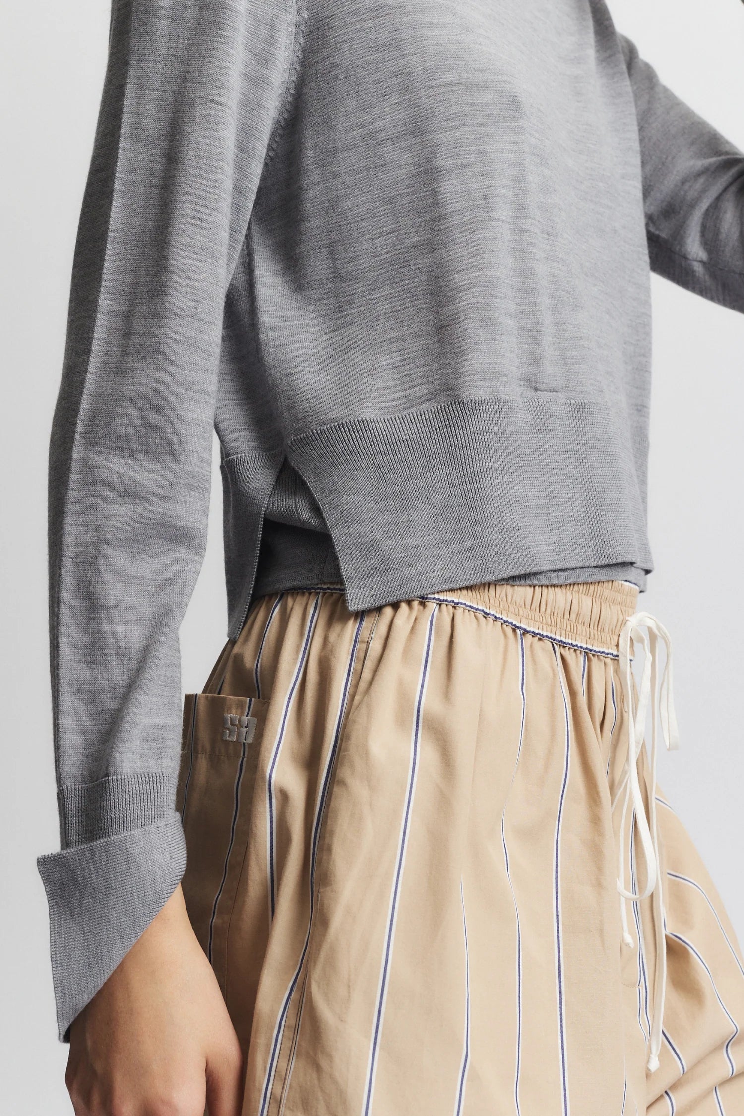 Person wearing a gray sweater and beige striped pants on a plain background