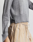 Person wearing a gray sweater and beige striped pants on a plain background