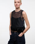 A blonde model wearing a black sheer mesh sleeveless top with a feathered hem, paired with dark blue jeans, against a plain light gray background.