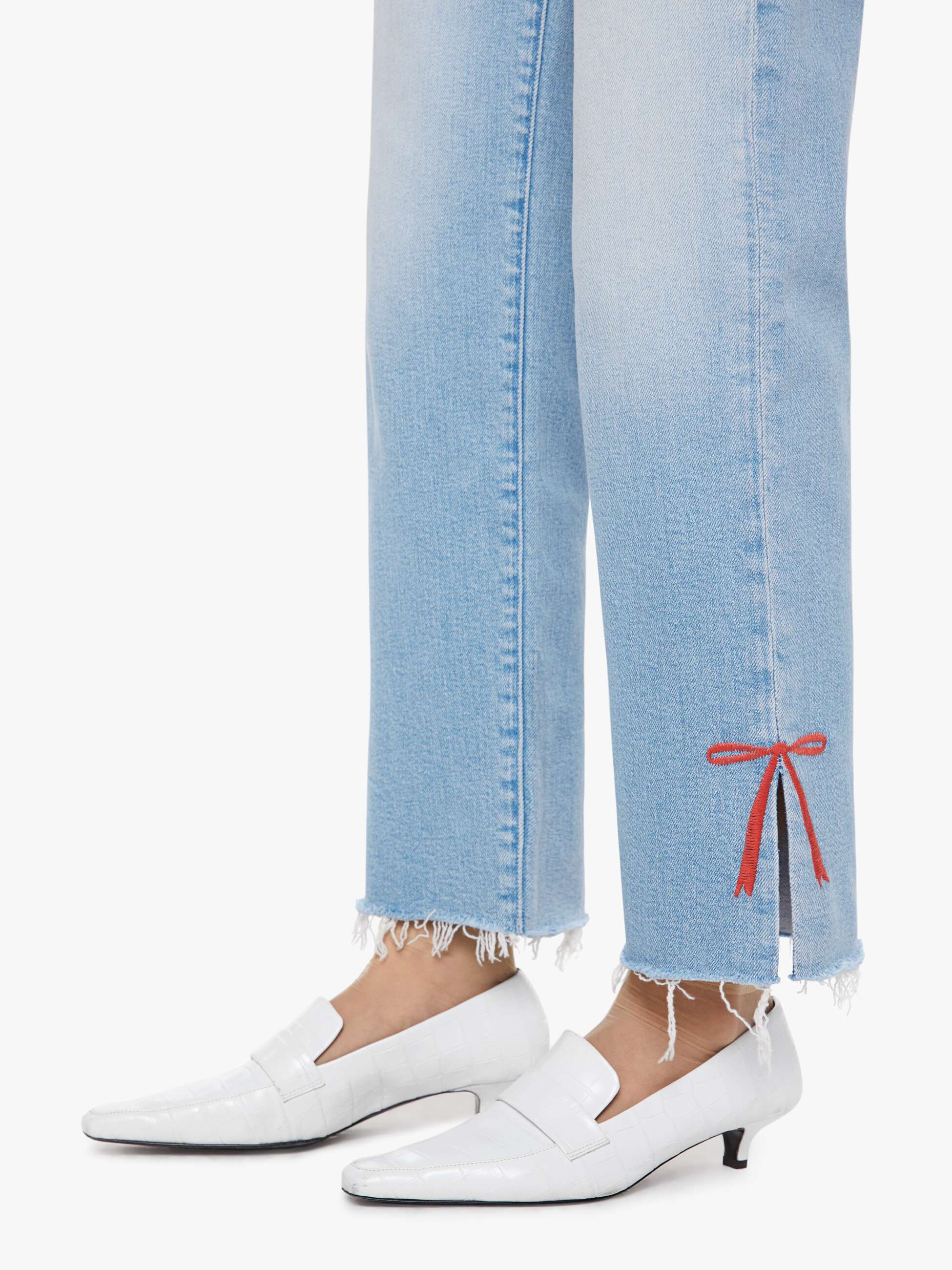 White loafers worn with light blue jeans on a white background