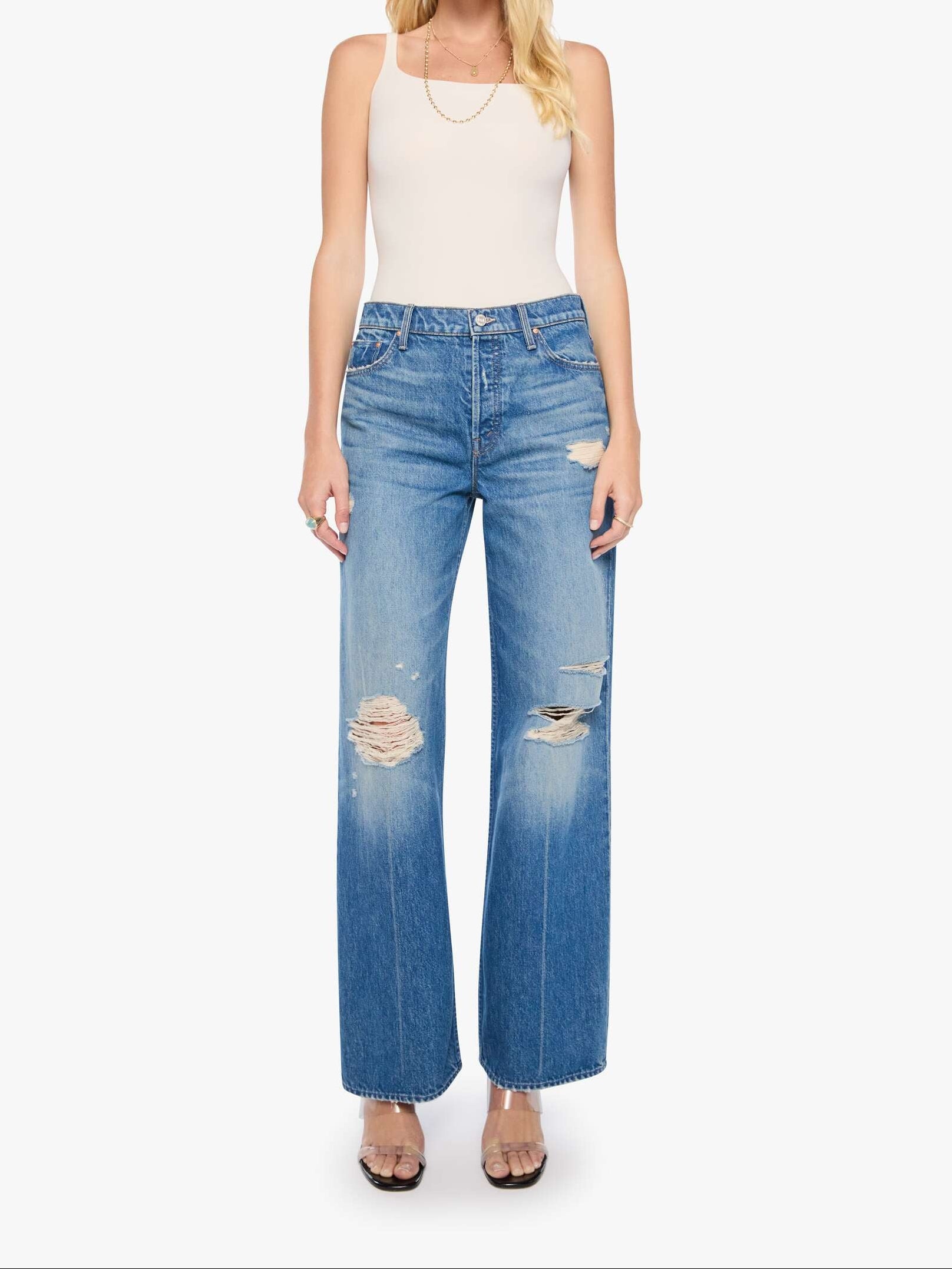 A woman modeling a pair of high-waisted, wide-leg blue jeans with distressed details and a faded wash, paired with a white tank top and sunglasses against a plain white background.