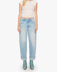 A woman modeling light-wash blue jeans with a cream ribbed crop top and green snakeskin boots, standing against a plain white studio background.