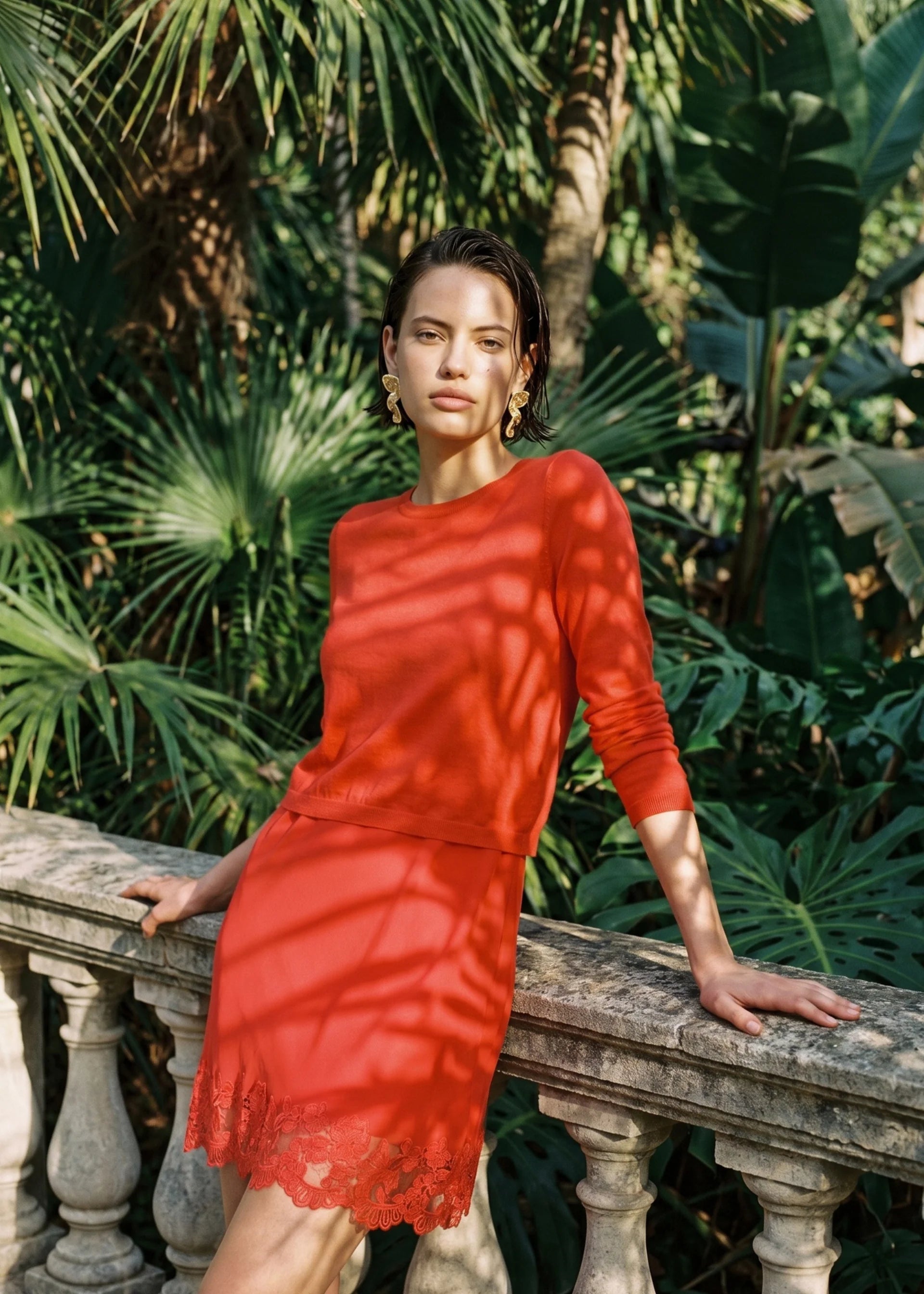 Woman in a red set standing against a backdrop of green foliage.