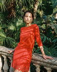 Woman in a red set standing against a backdrop of green foliage.