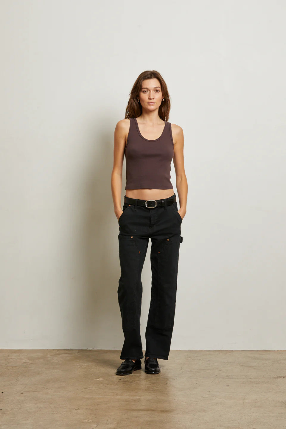 Woman wearing a brown tank top and black pants against a plain background front view