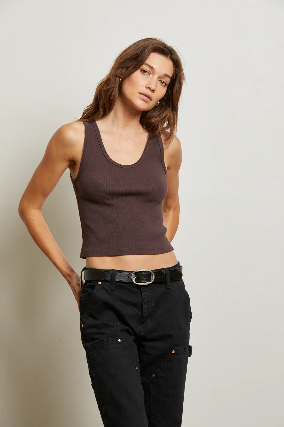 Woman wearing a brown tank top and black pants against a plain background front view