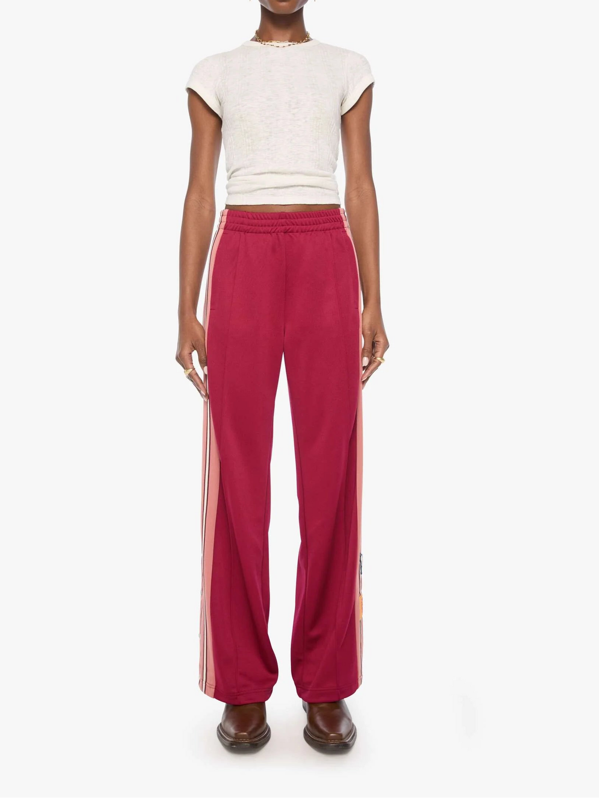 A model stands against a plain white studio background wearing a cream short-sleeve knit crop top and RED wide-leg pants with orange side stripes.