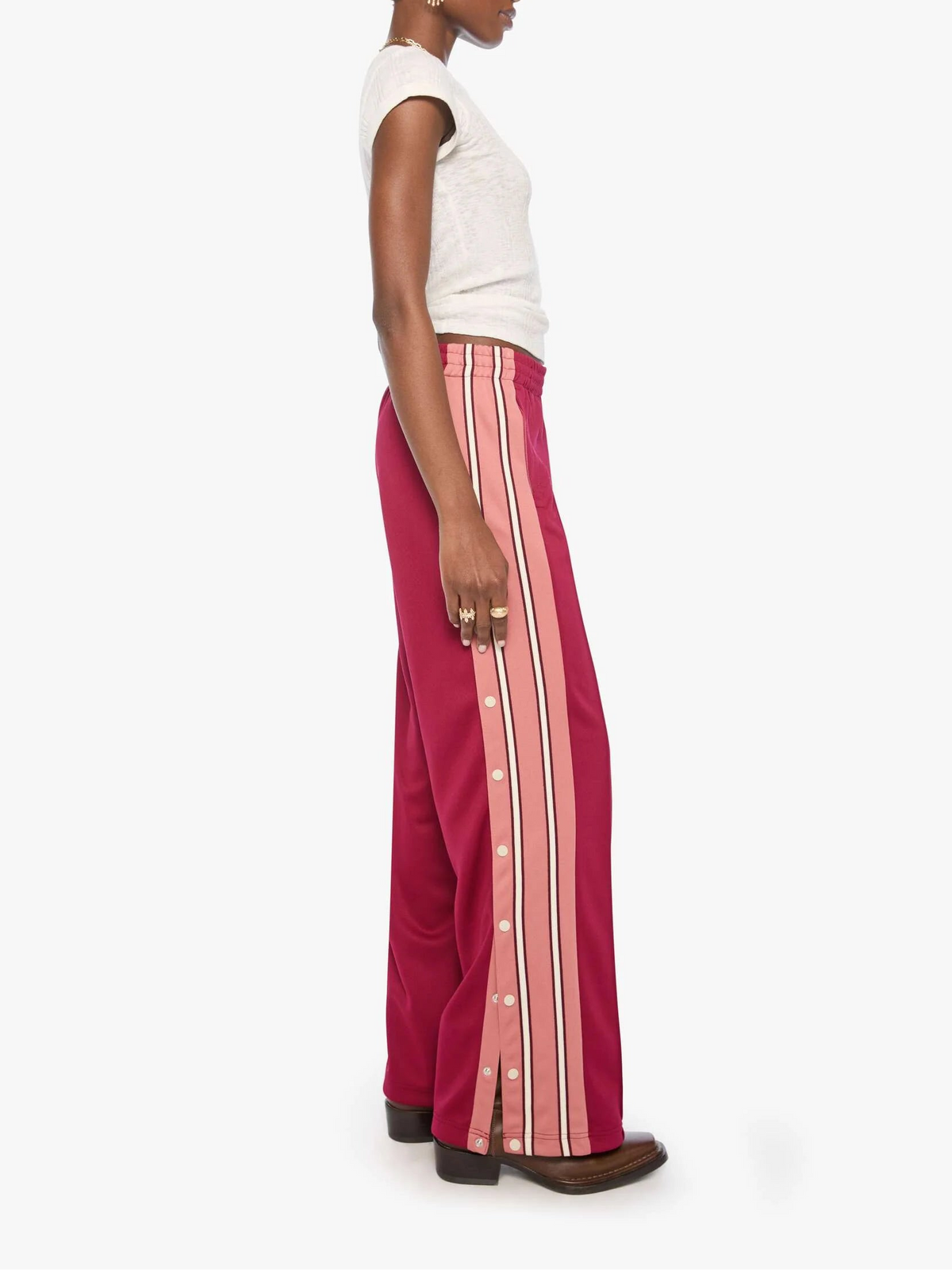 A model shown in profile wearing a white sleeveless top and high-waisted, wide-leg magenta trousers with vertical pink and white stripes down the sides, set against a plain light gray background.