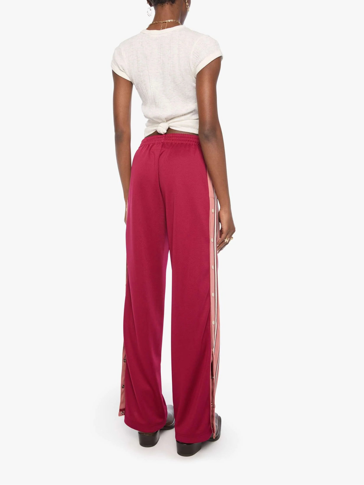 A model shown from the back wearing bright magenta wide-leg pants with white side stripes, paired with a white short-sleeve top, against a plain white background.