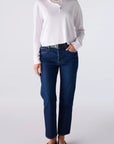 A model wearing a white long-sleeve henley shirt, dark blue straight-leg jeans, a black belt, and black flats, standing against a light gray studio background.