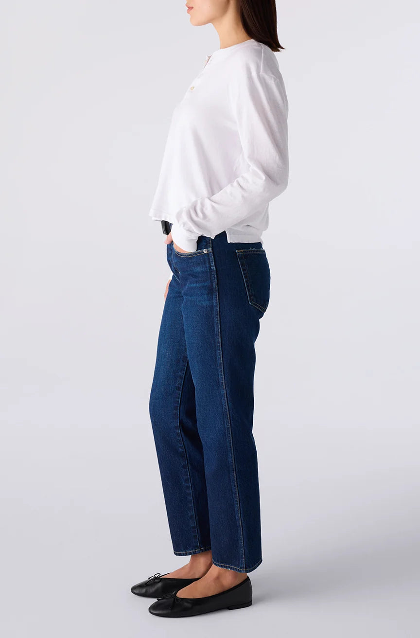 Person wearing a white sweater and blue jeans on a light gray background