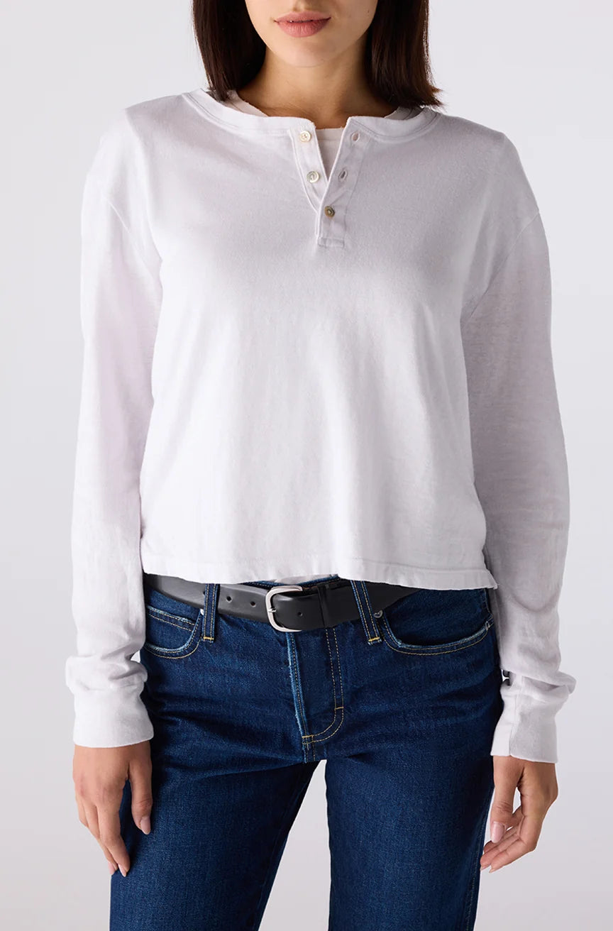 Person wearing a white long-sleeve henley shirt and blue jeans on a plain background