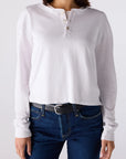 Person wearing a white long-sleeve henley shirt and blue jeans on a plain background
