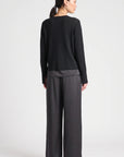 model wearing a black vneck sweater over a silky black top with black pants on a grey background, back view