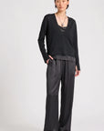 model wearing a black vneck sweater over a silky black top with black pants on a grey background