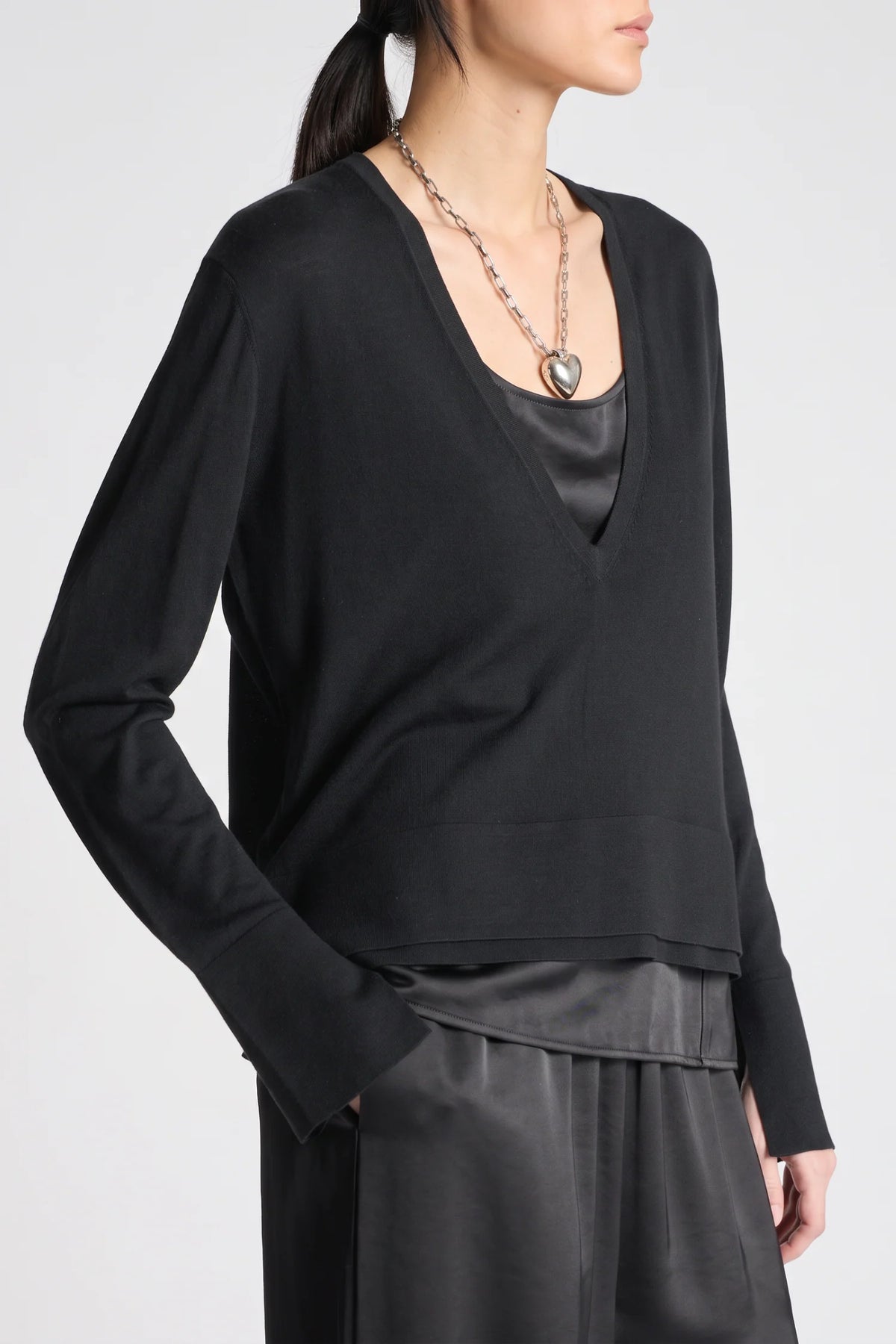 model wearing a vneck sweater over a silky black top with black pants on a grey background