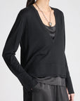 model wearing a vneck sweater over a silky black top with black pants on a grey background