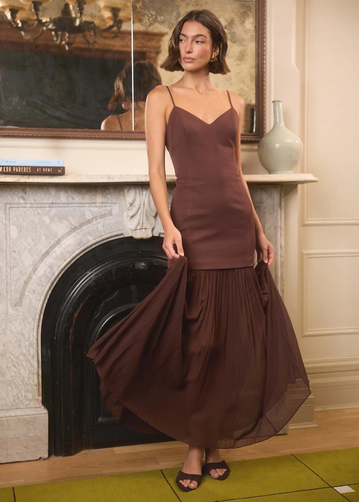 model wearing a brown dress with a fireplace and artwork in the background 