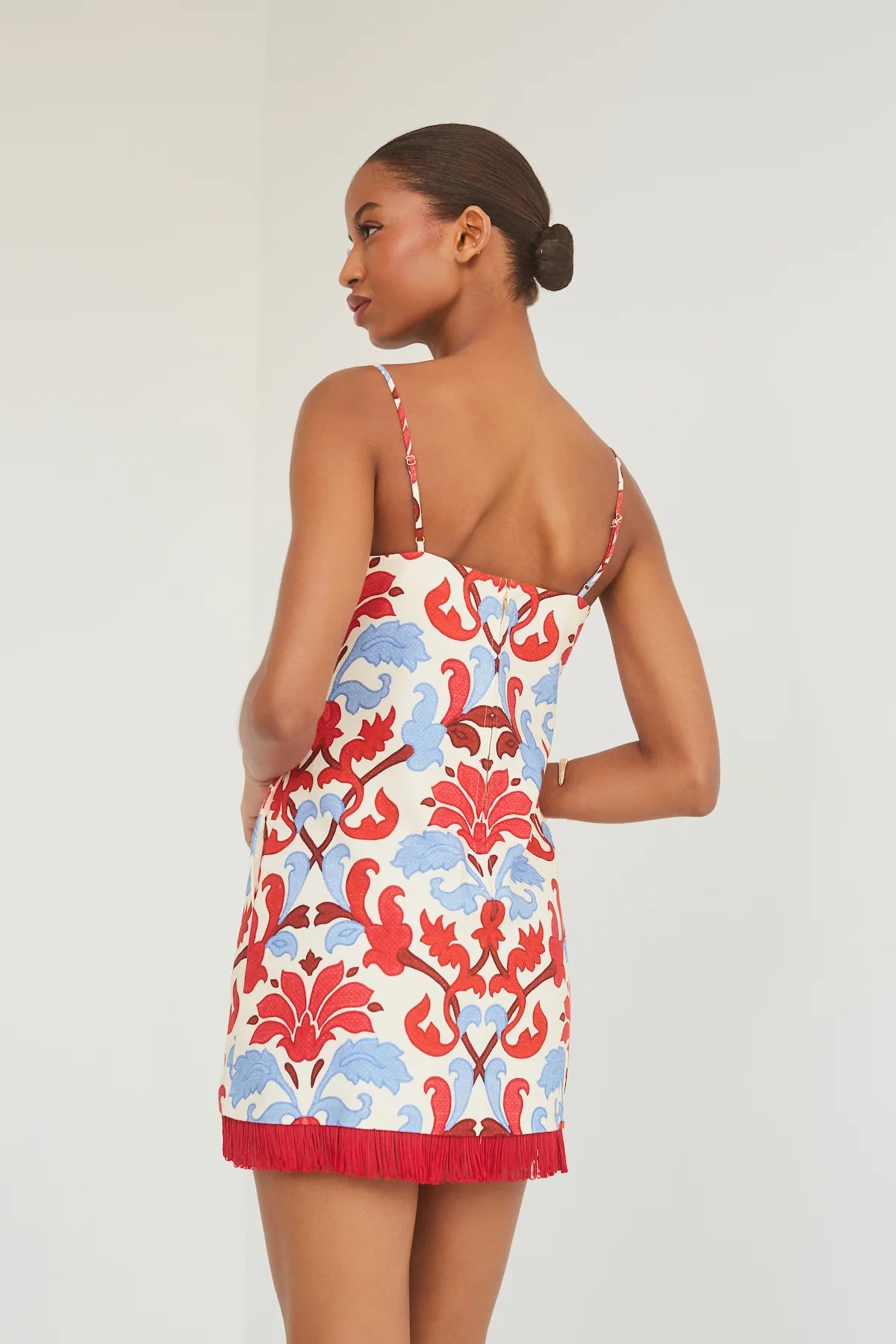 Woman wearing a floral dress with red, blue, and ivory pattern on a white background, back view