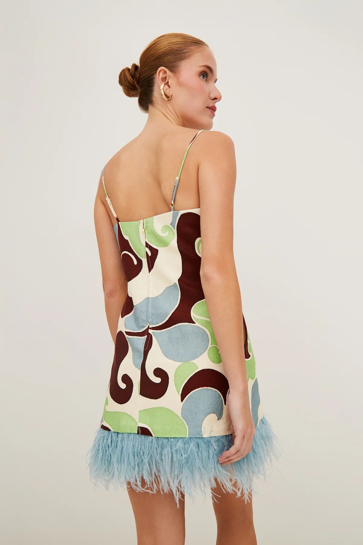 Woman wearing a patterned dress with frayed hem on a plain background, back