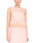 A model wearing a sleeveless light pink dress with a sheer mesh bodice, a feathered ruffle trim at the waist, and a flowing skirt, shown against a plain white background.