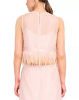 A woman shown from the back wearing a sleeveless blush pink dress with a sheer upper back panel, feathered trim at the waist, and a flowing skirt against a plain white background.