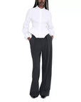 A model wearing a white long-sleeve button-up shirt with a structured peplum waist and black wide-leg trousers, standing against a plain white background.